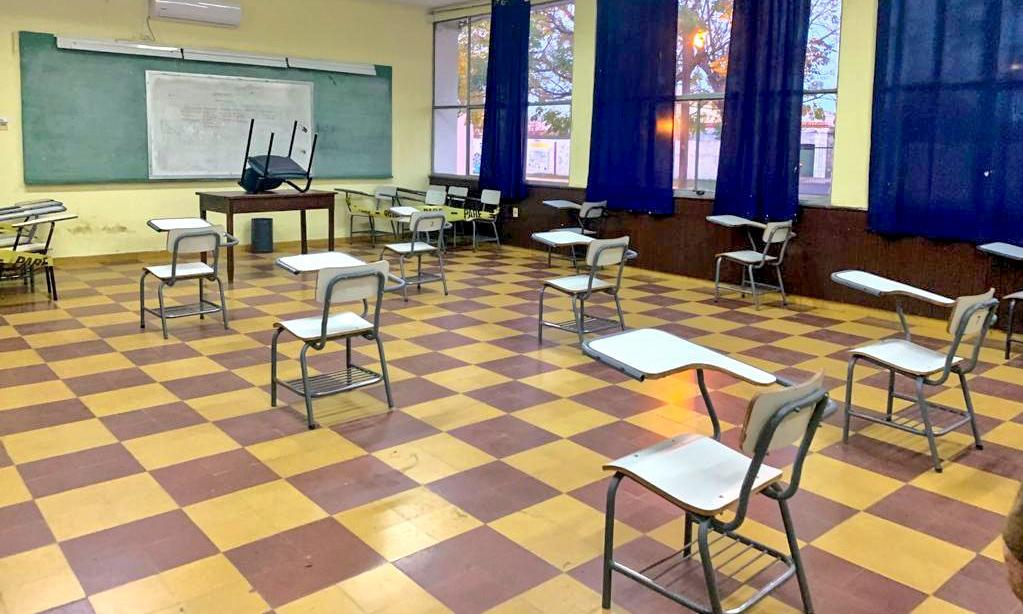 Salón de clases vacío con bancos distanciados.