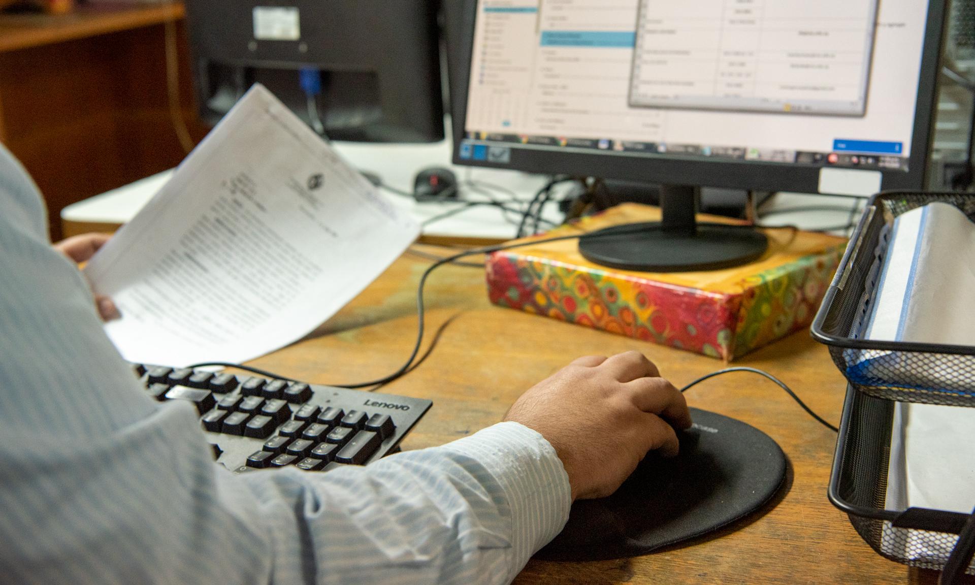 Administrativo en un escritorio de trabajo sosteniendo documentos y utilizando una computadora.