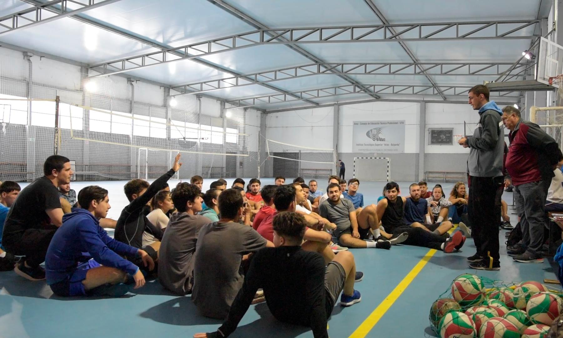 Docente y estudiantes durante clase de Educación Física dentro de un gimnasio.