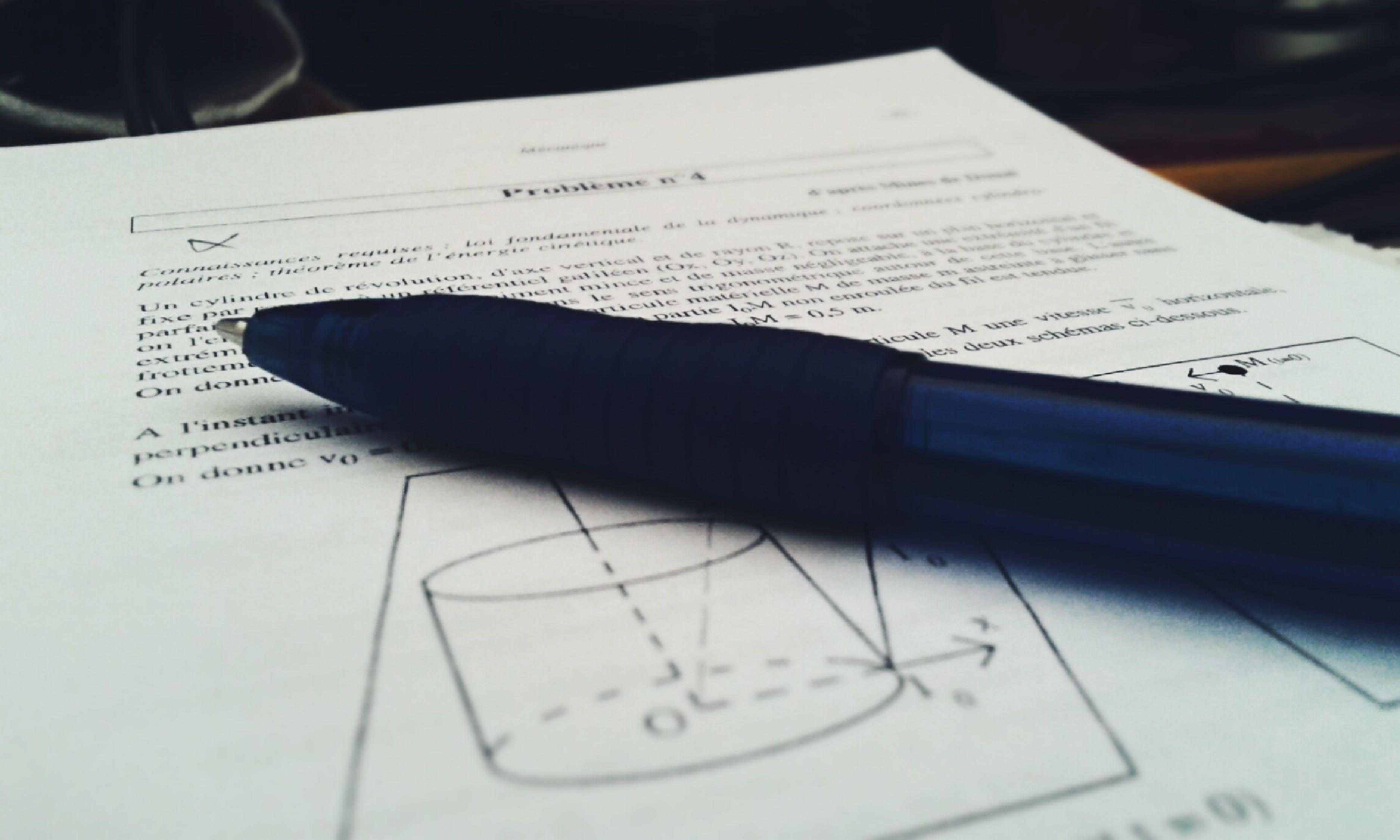 Bolígrafo encima de un papel con ejercicio teórico de Física.